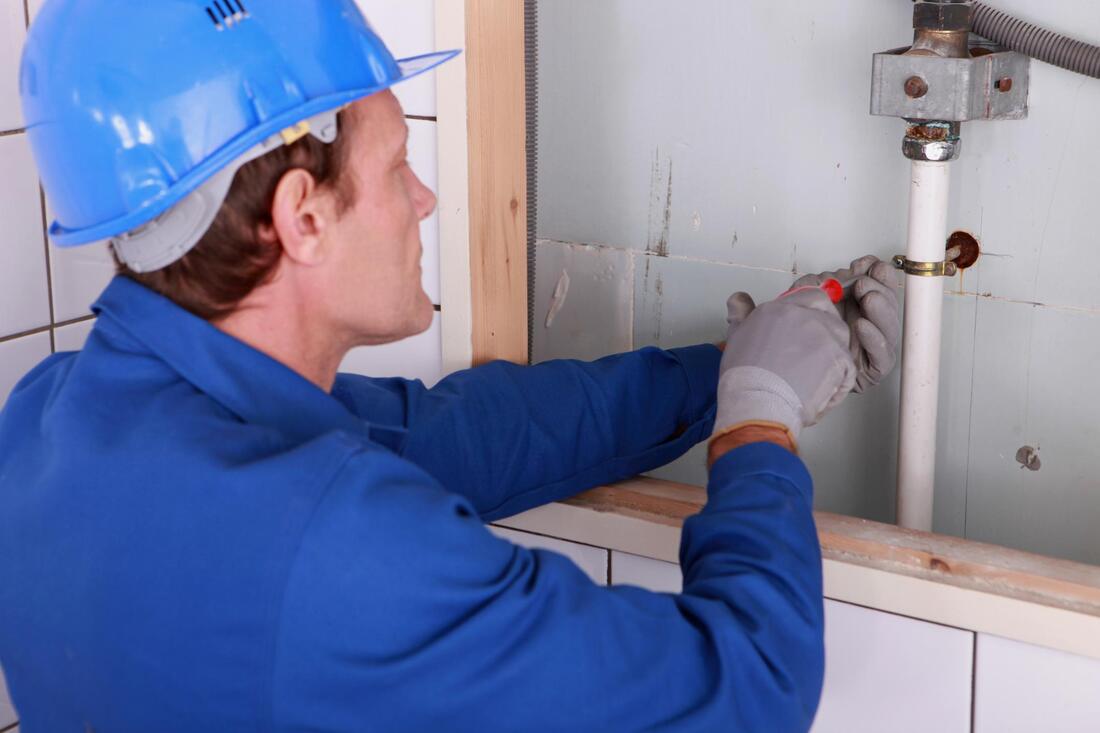 a commercial plumber tightening a bracket on a job